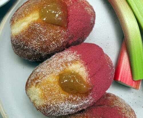 Three vegan doughnuts with pink and white sugar next to rhubarb, from Pipp & Co