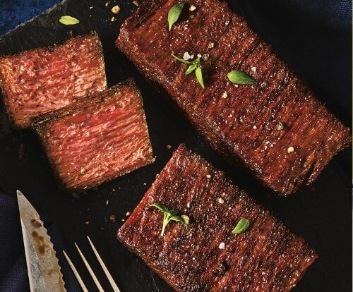 Two Aldi vegan steaks on a black plate. One of them is cut up, showing a pinky centre