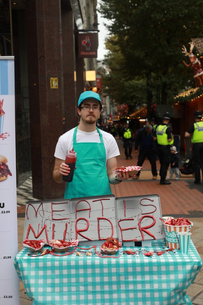 An activist at a fake chicken stall with the words "Meat is Murder" written on it