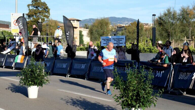 PETA supporters holding up a banner reading "Stop supporting orca abuse. Drop marine parks!" on the sideline of a marathon as the TUI CEO runs past