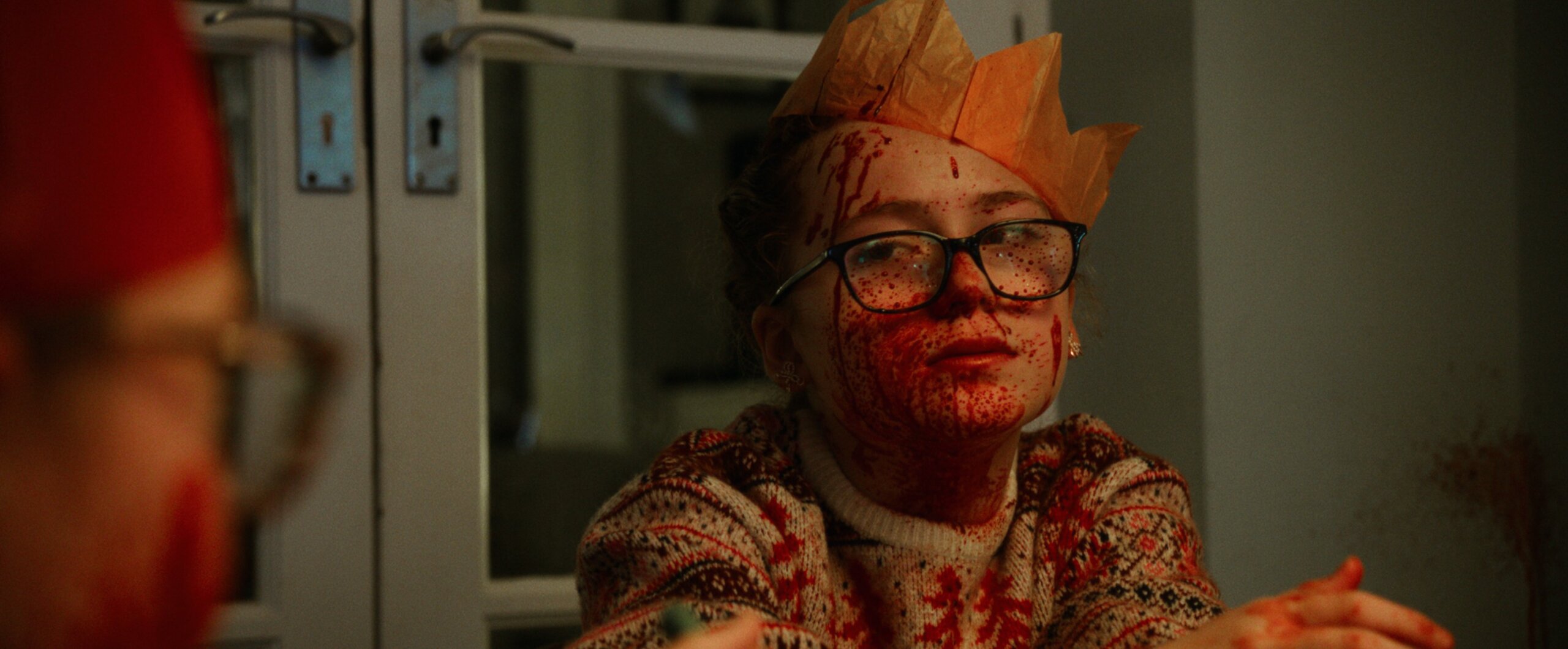 A child sitting at a Christmas table covered in fake blood and wearing a Christmas hat