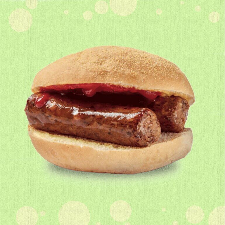 A Greggs vegan sausage breakfast roll in front of a green background