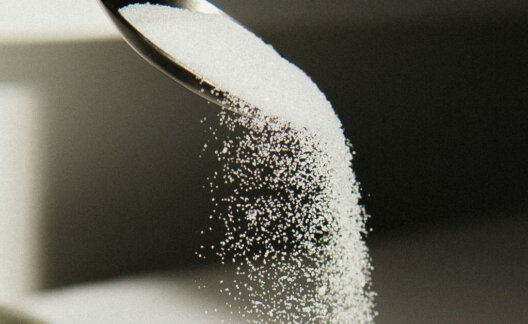 A black spoon pouring white sugar into a bowl