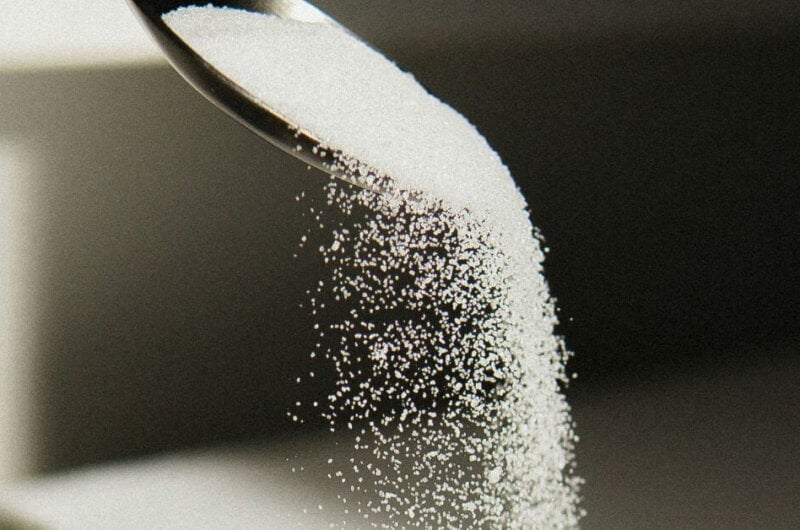 A black spoon pouring white sugar into a bowl